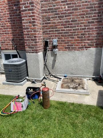 New Carrier condenser staged next to refrigerant tools on lawn beside brick building
